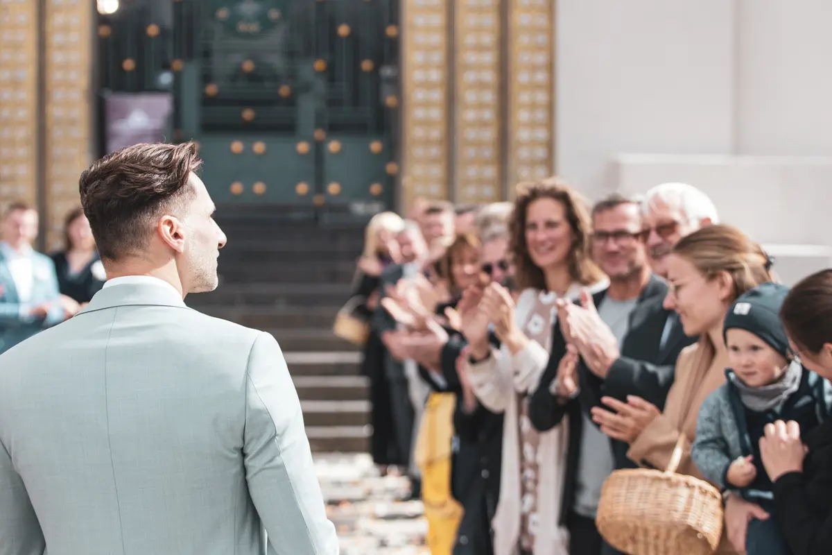 Bräutigam am Eingang des Standesamts, während die Gäste applaudieren