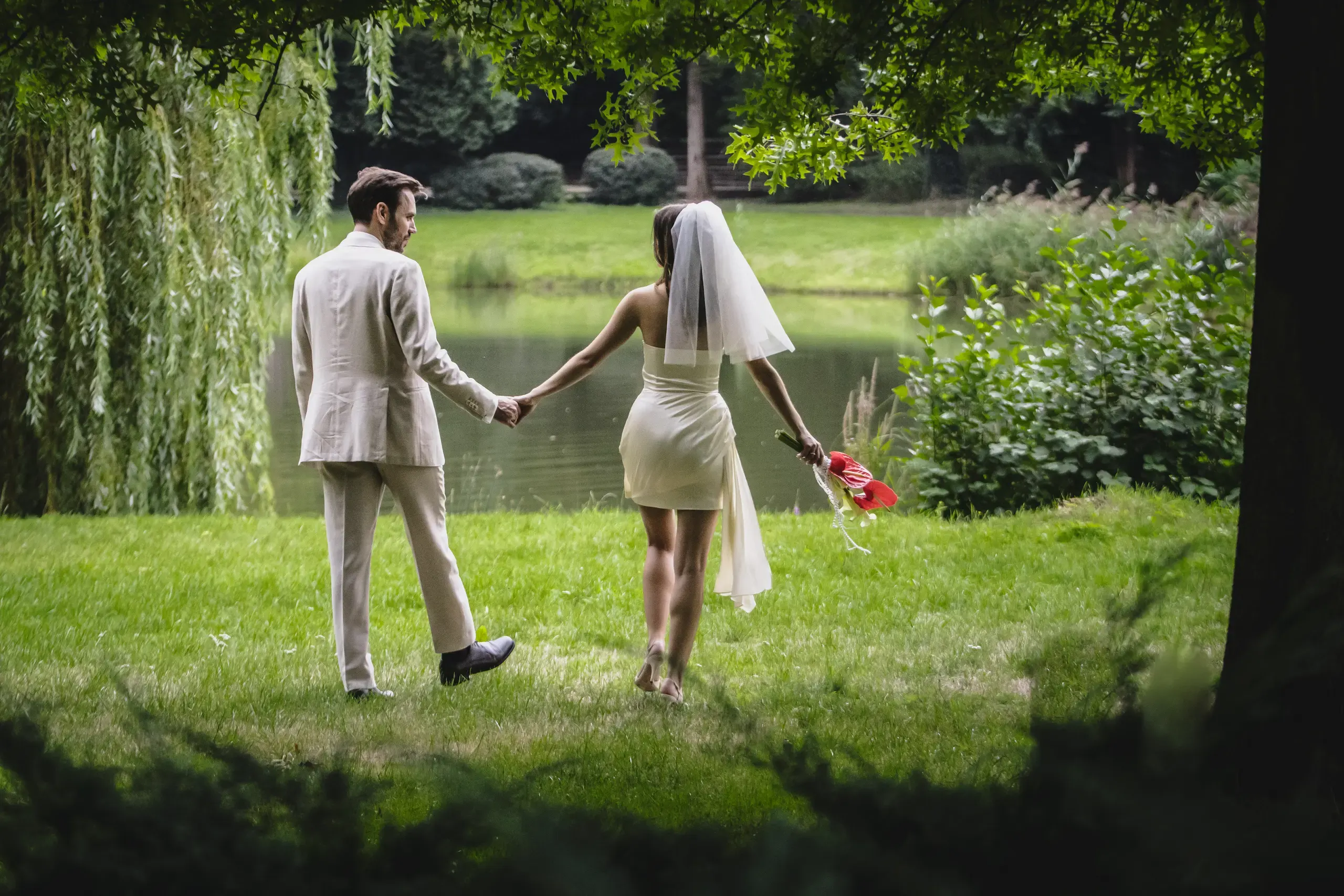 Brautpaar geht Hand in Hand zum Teich im Schlosspark – Hochzeitsbilder im Grünen